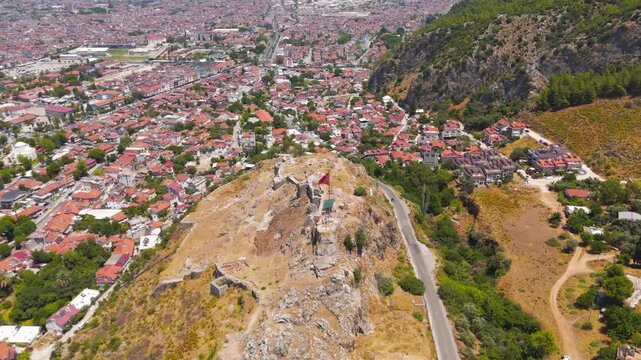Fethiye, Turkey. Large Turkish flag flying on flagpole atop the historic Fethiye Castle hill with ancient Lycian rock cut tombs in the surrounding cliffs, drone footage.. Aerial View, MasterShots, Sp