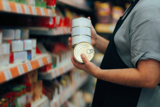 Supermarket Employee Stocking Shelves with food Cans in grocery Store. Retail worker organizing shelves ensuring a well stock inventory in a store