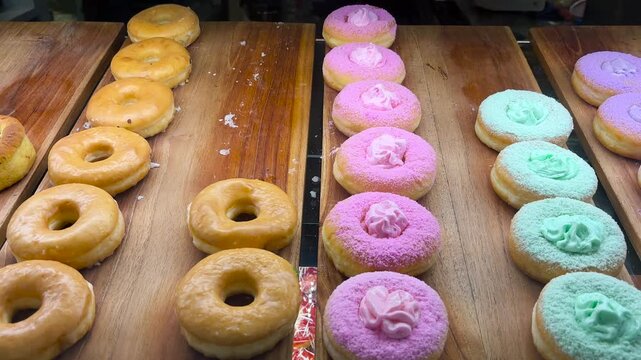 A variety of donut flavors in a cake display case. Sweet donuts with a variety of topping colors.