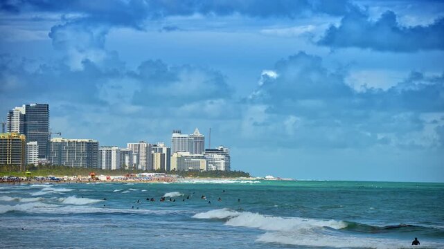 Ocean waves and skyline of Miami Beach under cloudy sky. Wide angle view of Atlantic ocean waves with South Beach cityscape under dramatic blue clouds.