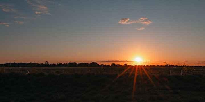 Golden sunset over a rural field with dramatic sunbeams piercing the horizon