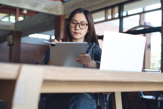 Focused woman using digital tablet with laptop on desk, remote working in modern office, studying or working with digital devices. Close up