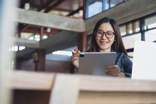 Smiling woman using tablet and stylus in modern office, working online with laptop in bright, contemporary workspace.