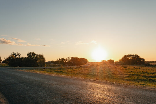 Golden hour sunset over a rural landscape with a bitumen road leading into the distance