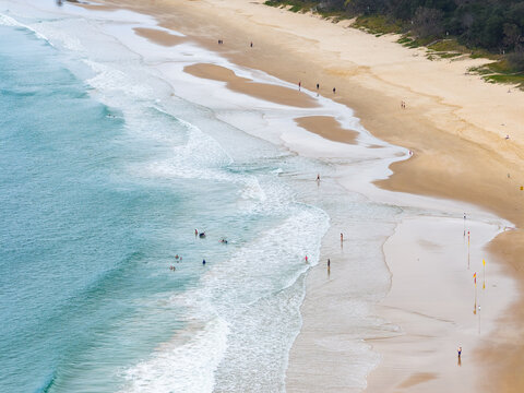Aerial view of people walking through gentle waves rolling onto a sandy beach