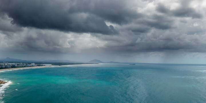 Aerial panorama view of rain falling from dark clouds over a calm turquoise sea and distance hills