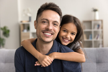Obraz premium Loving daughter cuddle handsome father, family sit on sofa, posing for camera, with positive, joyful expression, relish priceless moments together, feel unconditional love, close up. Happy fatherhood