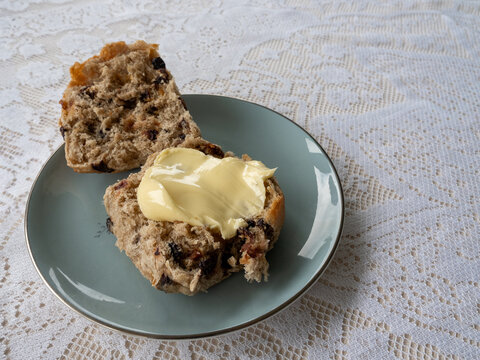 Hot cross bun with butter on a blue plate with lace table cloth