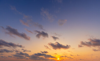 Beautiful sunset sky with golden light and purple clouds over the horizon,Dramatic sunset sky background with soft orange sunlight and scattered dark clouds during twilight. The evening atmosphere.