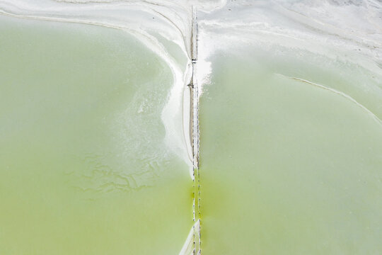 Aerial view of crusty edges around a fenceline running through a pastel green salt lake