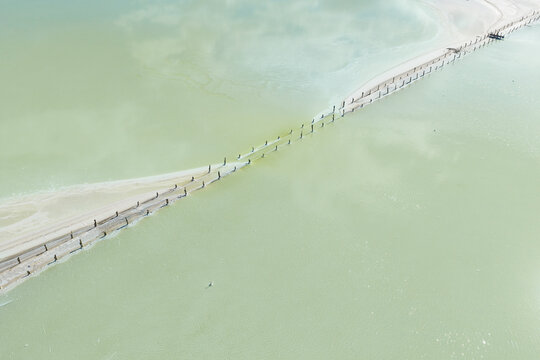 Aerial view of crusty edges around a fenceline running through a pastel green salt lake