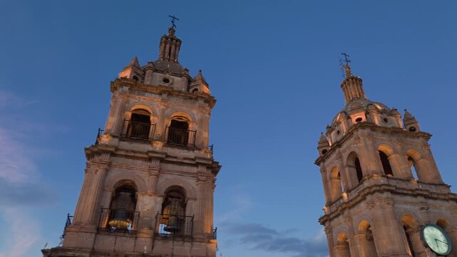 Cathedral Basilica of Immaculate Conception in Durango, Mexico at sunset. Twin bell towers with ornate baroque architecture illuminated by warm golden light against blue twilight sky with pink clouds.