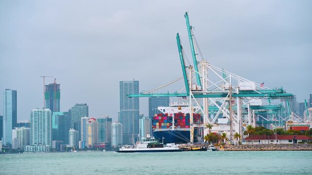 Miami, USA, 9 April 2026: Large cargo ship at PortMiami with industrial shipping cranes. Heavy machinery cranes loading container ship at sea port with downtown Miami skyline in the background.