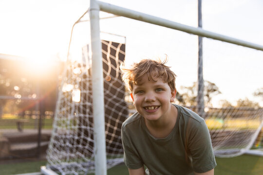 blonde boy smiling and leaning forward in front of a soccer goal