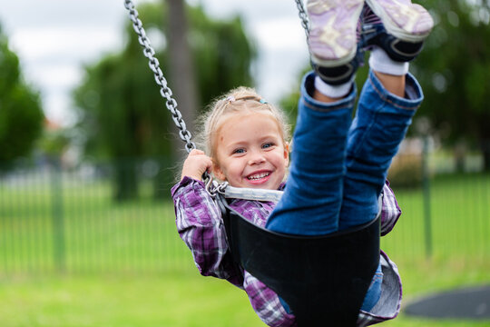 Happy little girl playing on swing at park on overcast day in Glen Innes