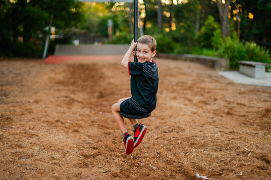 A young boy enjoys swinging at a park as the sun sets in the background, dressed in a rugby uniform