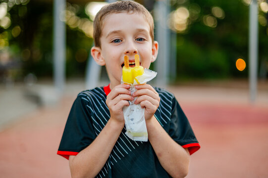 Child holds ice block and smiles while wearing a rugby uniform in an outdoor setting