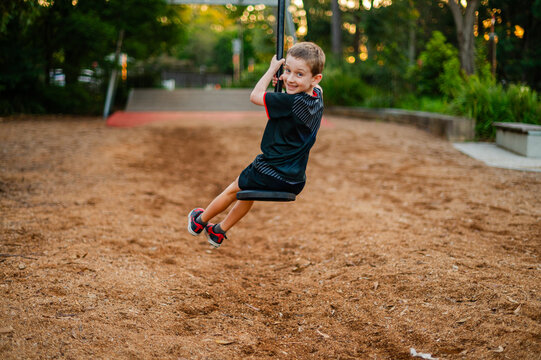 A young boy swings at a park, enjoying playful moments in a rugby outfit as the sun sets