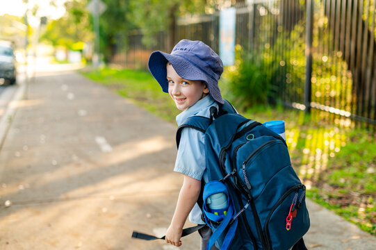 A boy walks along a path on his way home from school, wearing a backpack