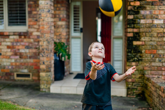 A boy in a rugby uniform is playing with a rugby ball outside his home