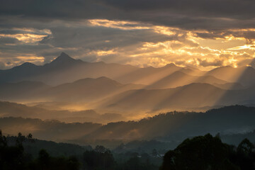 Obraz premium Timelapse of golden sunrise emerging behind mountain range, soft clouds moving, light rays spreading across landscape