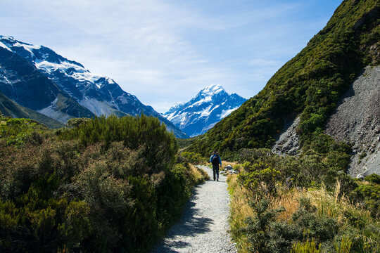 Person in the distance walking along a track in a glacial valley with snow capped mountains
