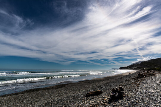 A stoney beach and ocean scene with streaky cloud patterns and dramatic lighting