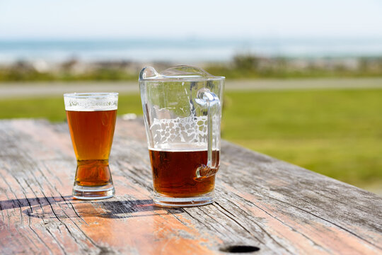 Jug and glass of beer on an outdoor table with blurred background of lawn, sea and sky
