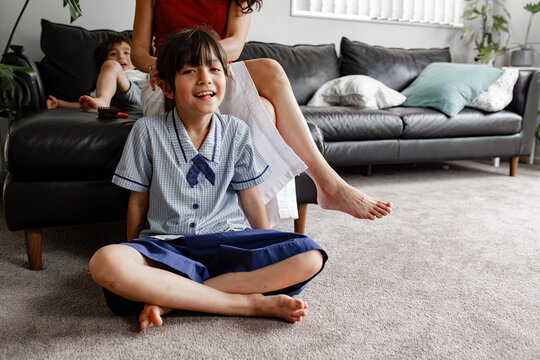Young girl sitting on carpeted floor while mum is tying her hair