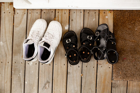 Three pairs of footwear neatly arranged on a wooden deck beside a brown doormat