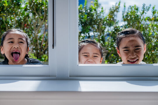 Three kids pressing their heads and one sticking his tongue out against the glass window outdoors