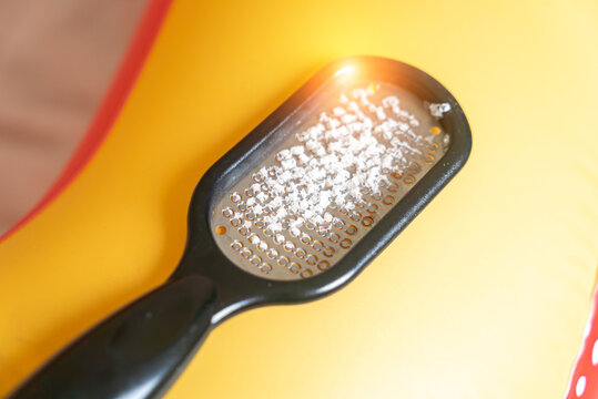 Close-up of a black foot file covered with white dead skin flakes after callus removal, resting on a bright yellow background.