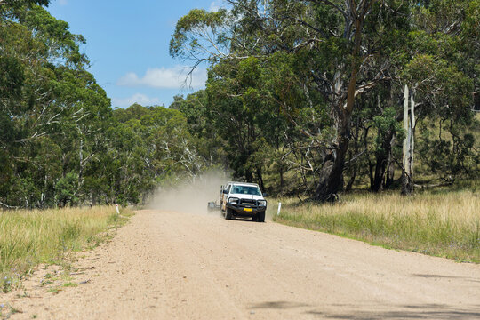 Car pulling trailer traveling down remote gravel road through bushland