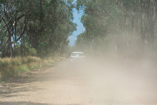Car kicking up dust while traveling down remote gravel road through bushland