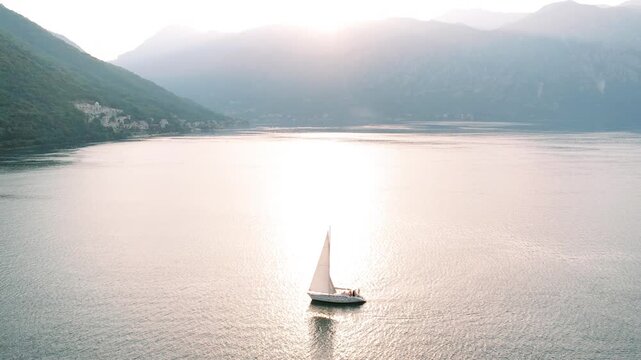 Peaceful sailing scene. Gentle sailboat glides over placid bay as evening sunlight reflects beautifully on water