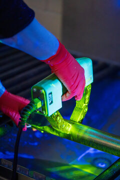 Magnetic particle inspection MPI test using an AC yoke on a metal component glowing green under ultraviolet light. A technician performing non-destructive testing NDT procedure in dark industrial lab
