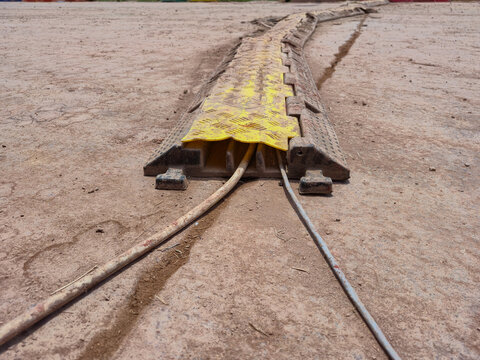 ​Outdoor yellow and black heavy-duty rubber cable protector ramp on dirt ground, shielding electrical wires to prevent trip hazards and ensure safety