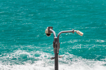 Obraz premium Security surveillance cameras on metal pole above turquoise sea with waves
