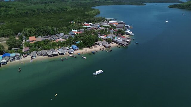 Drone establishing shot of coastal village in Koh Jum Thailand with fishing boats along tropical shoreline calm blue water and green hills in background ideal travel and nature footage.