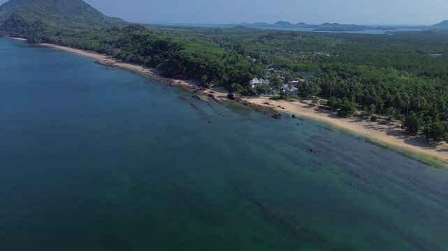 Cinematic drone shot of remote jungle coastline on Koh Jum and Koh Pu in Krabi Thailand featuring rugged shoreline tropical forest and a distinct island mountain ridge and islands in the distance.