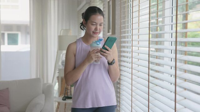 Young gen z active woman drink whey creatine shake bottle eating diet food using phone calorie plan app after home sport workout. health care asia people happy relax protect aging life weight loss.