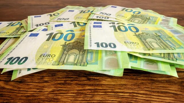 Pile of one hundred euro banknotes on wooden table. Cash background representing wealth, success and financial profit, 4k
