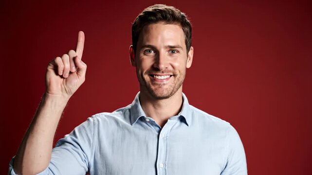A young man in a light blue shirt smiles and points his finger up, expressing a moment of realization or success.