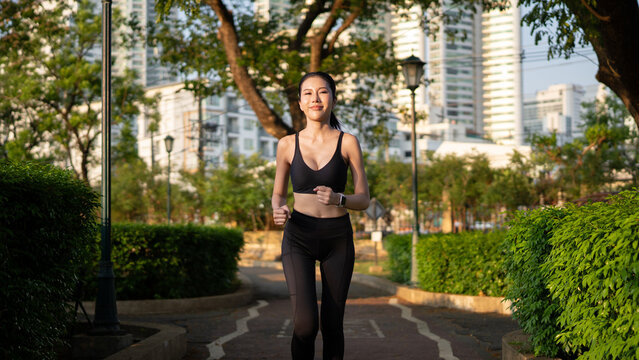 Happy slim woman wearing sportswear jogging in the city at sunrise. Young beautiful asian female in sports bra running outdoor. Workout exercise in the morning. Healthy and active lifestyle concept