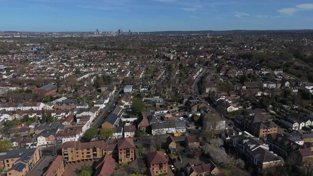 Croydon skyline at the distance on a sunny day. Aerial view from Sutton in Surrey, UK. Flying forward above urban area with multiple houses and streets with light traffic.