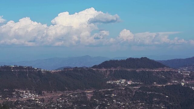 Right Pan of Mountain Ranges and Hill Station Under Large Cumulus Clouds. A smooth horizontal camera pan from left to right, showcasing layers of misty mountains and a scattered hill station