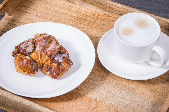 Traditional croissants with poppy seed filling and cup of coffee with milk on wooden tray. Dessert from polish city Poznan. Martin's croissant