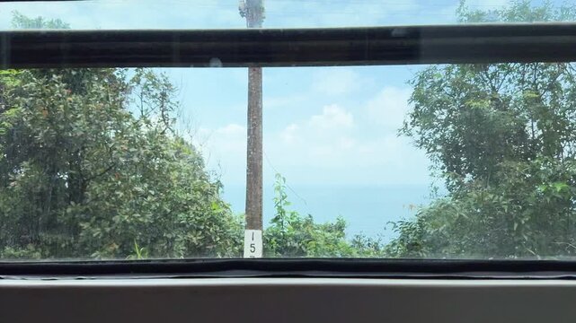 View through a moving train window past dense green vegetation in central Vietnam, capturing everyday rail travel, blurred countryside motion, and a quiet tropical landscape.