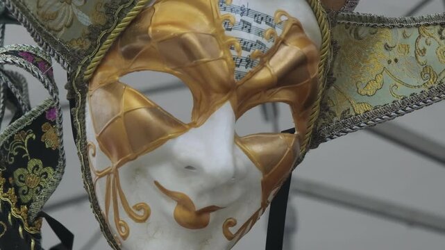 Static close-up of elegant golden Venetian masks adorned with musical notation in slow motion. Intricate theatrical costume pieces feature gold leaf patterns and decorative music symbols.