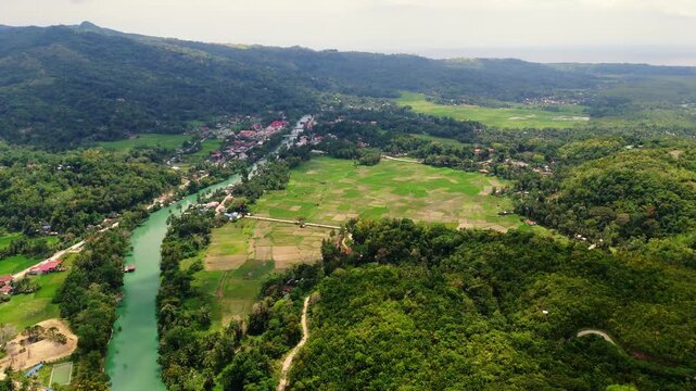 aerial view of the Loboc River valley and rural rice fields in Bohol. drone shot of winding river through tropical hills and agricultural farmland in Philippines